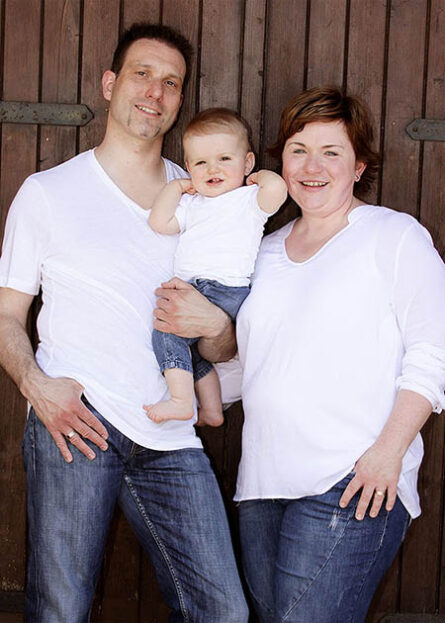 Familienfotos Fotoshooting Outdoor Mutter Vater Kind vor Holztor als Hintergrund