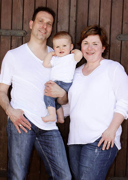 Familienfotos Fotoshooting Outdoor Mutter Vater Kind vor Holztor als Hintergrund